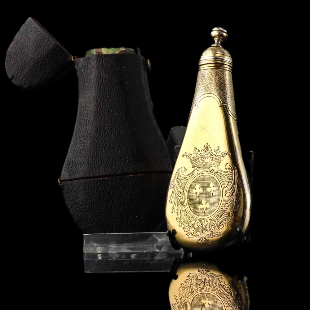 A seventeenth-century teardrop-shaped silver gilt scent flask engraved with a coronet and crest, positioned alongside its dark leather case. View II