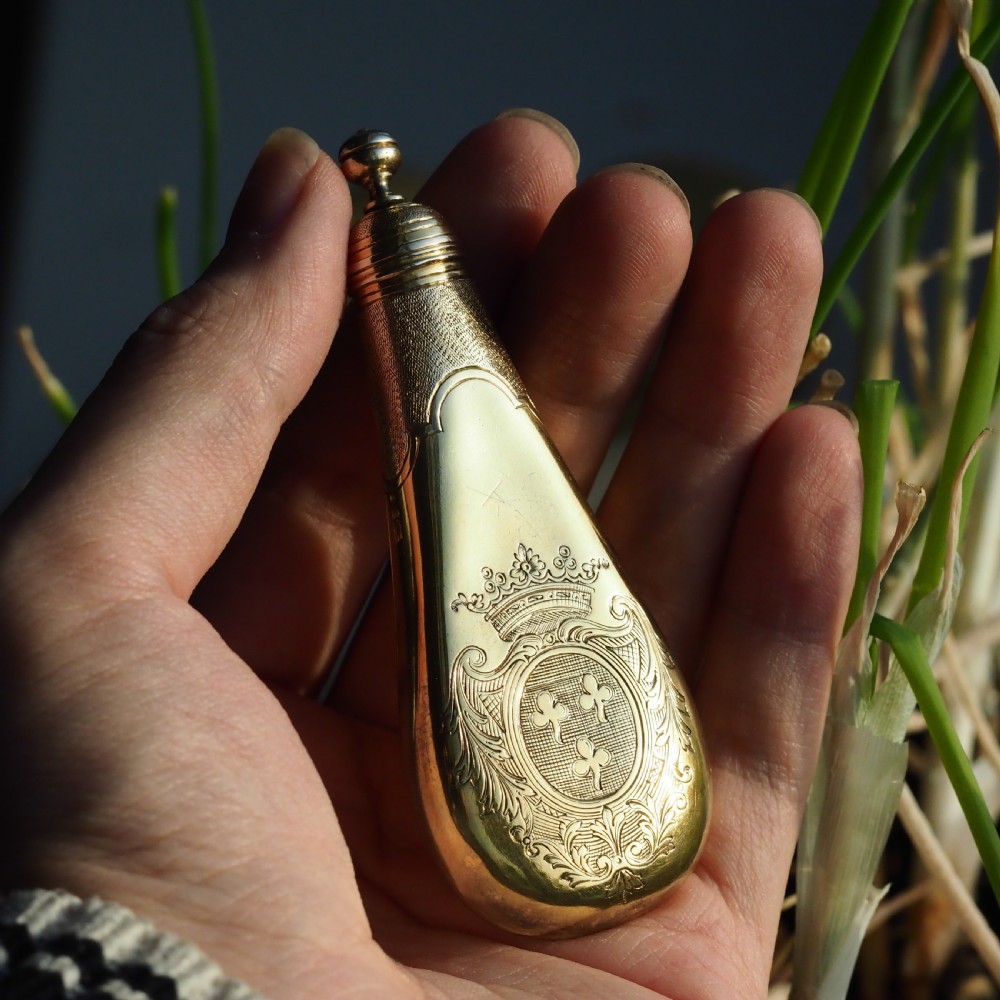 A seventeenth-century teardrop-shaped silver gilt scent flask engraved with a coronet and crest, positioned alongside its dark leather case. View VII