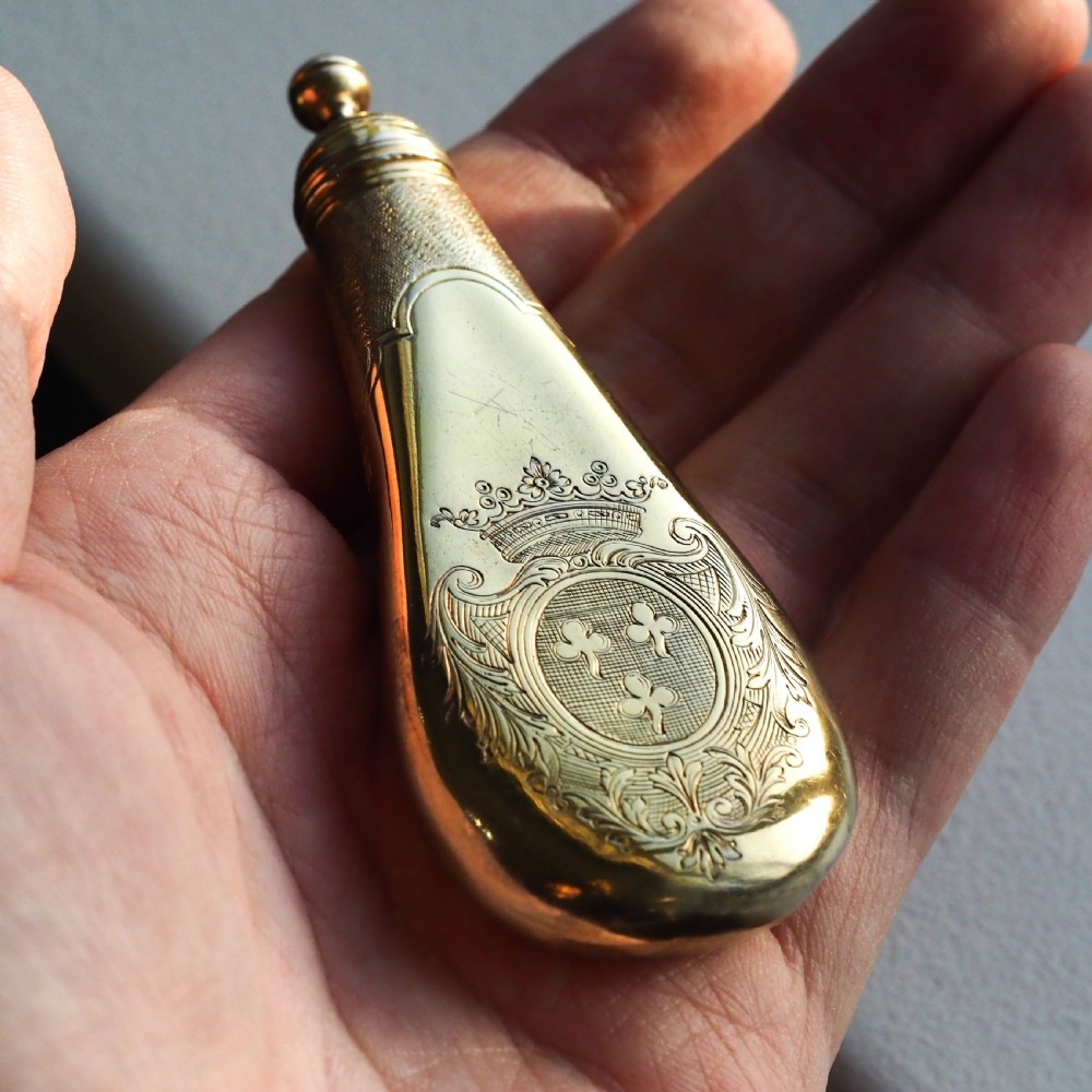 A seventeenth-century teardrop-shaped silver gilt scent flask engraved with a coronet and crest, positioned alongside its dark leather case. View VIII