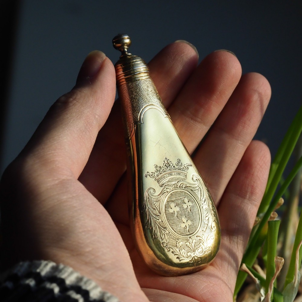 A seventeenth-century teardrop-shaped silver gilt scent flask engraved with a coronet and crest, positioned alongside its dark leather case. View IX