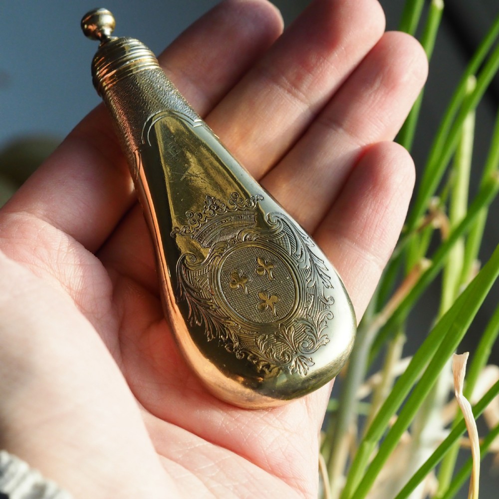 A seventeenth-century teardrop-shaped silver gilt scent flask engraved with a coronet and crest, positioned alongside its dark leather case. View X