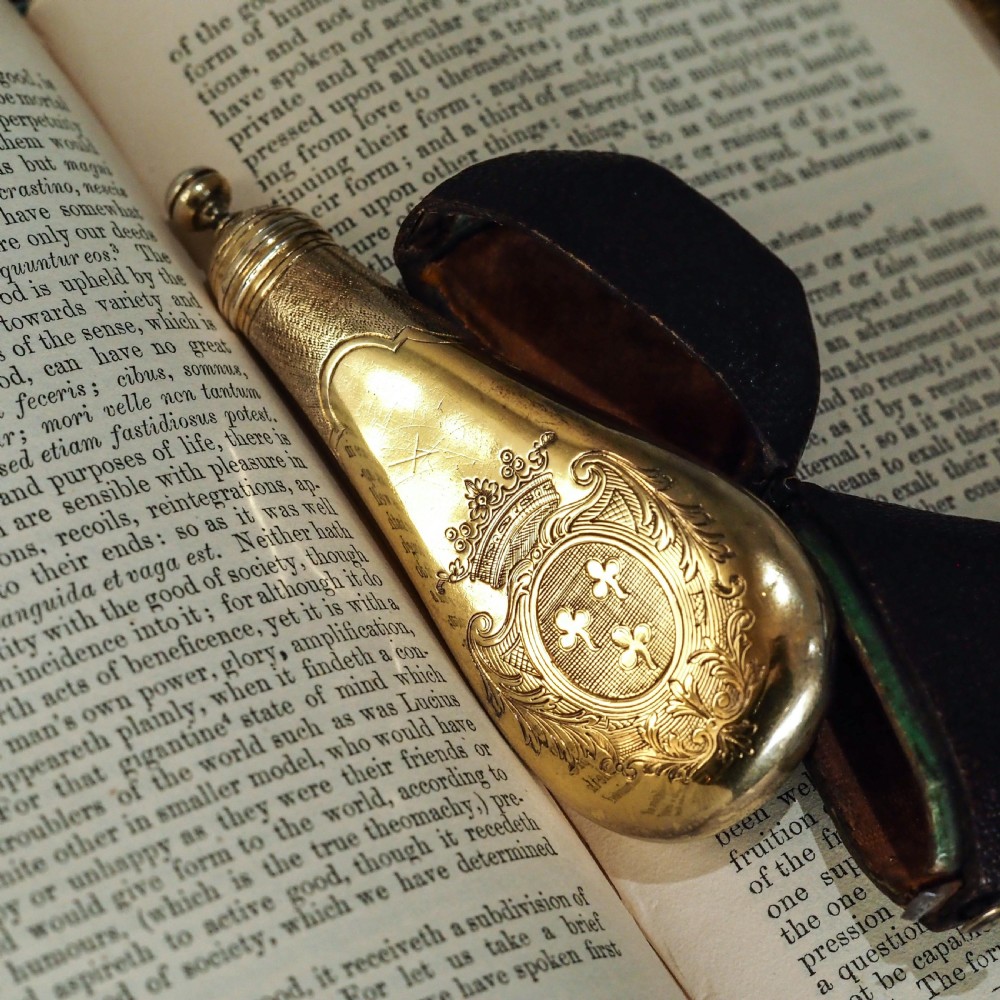 A seventeenth-century teardrop-shaped silver gilt scent flask engraved with a coronet and crest, positioned alongside its dark leather case. View XII