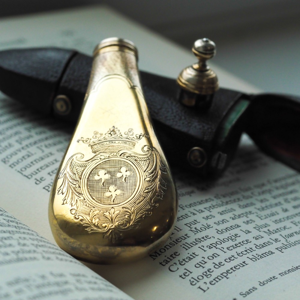 A seventeenth-century teardrop-shaped silver gilt scent flask engraved with a coronet and crest, positioned alongside its dark leather case. View XIV