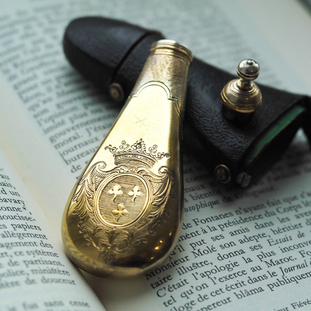 A seventeenth-century teardrop-shaped silver gilt scent flask engraved with a coronet and crest, positioned alongside its dark leather case. View XV
