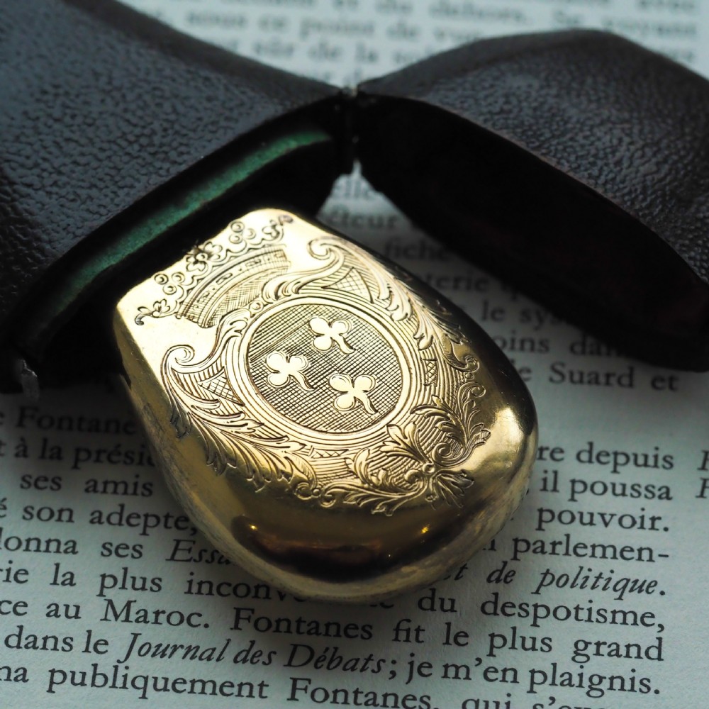 A seventeenth-century teardrop-shaped silver gilt scent flask engraved with a coronet and crest, positioned alongside its dark leather case. View XVII