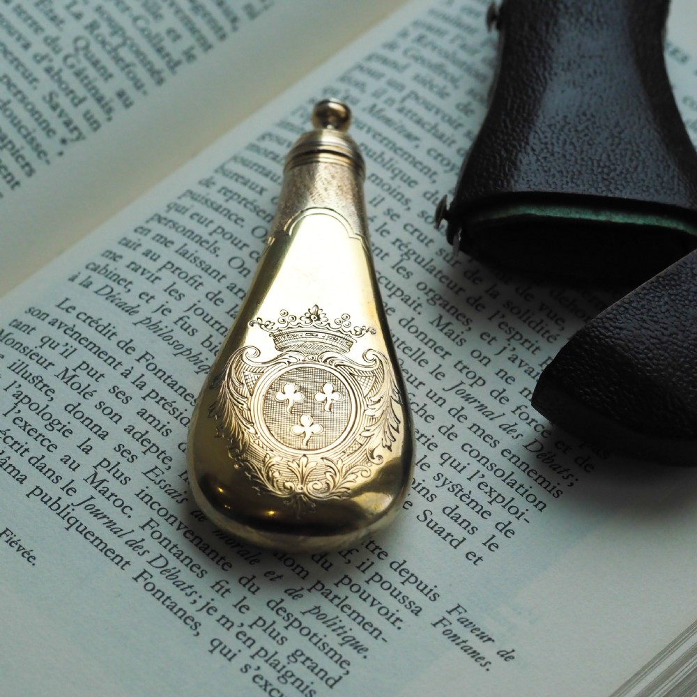 A seventeenth-century teardrop-shaped silver gilt scent flask engraved with a coronet and crest, positioned alongside its dark leather case. View XIX