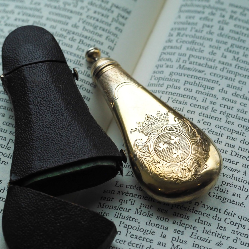 A seventeenth-century teardrop-shaped silver gilt scent flask engraved with a coronet and crest, positioned alongside its dark leather case. View XX