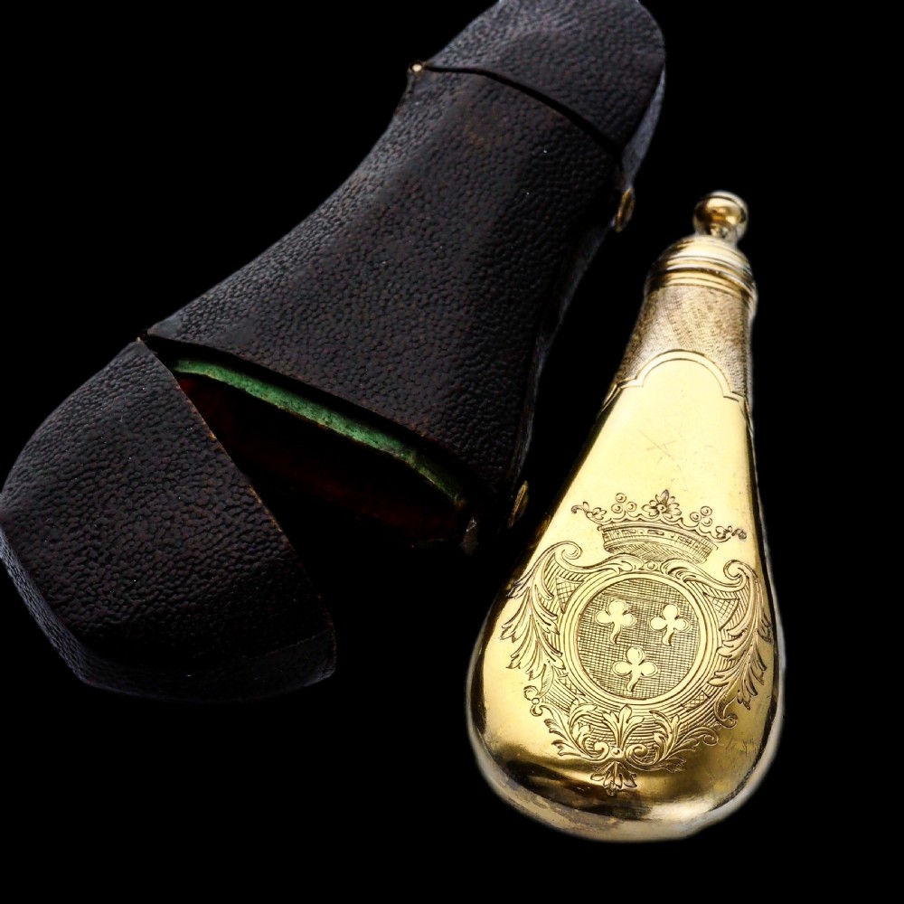 A seventeenth-century teardrop-shaped silver gilt scent flask engraved with a coronet and crest, positioned alongside its dark leather case. View XXVIII