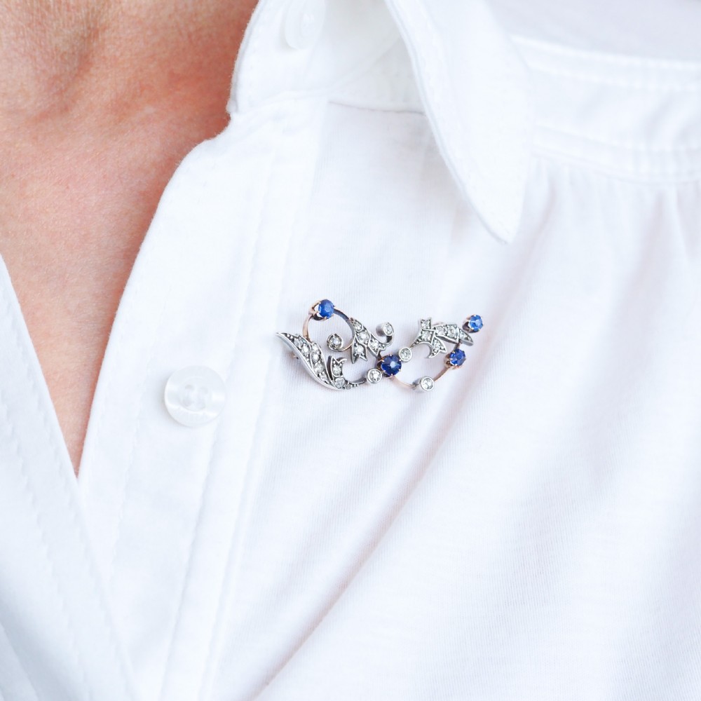 An antique Victorian foliate scroll brooch crafted in gold and silver, set with circular blue sapphires and accent diamonds. View V
