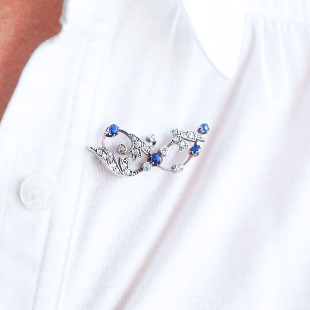 An antique Victorian foliate scroll brooch crafted in gold and silver, set with circular blue sapphires and accent diamonds. View VI
