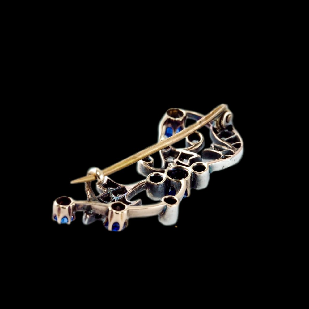 An antique Victorian foliate scroll brooch crafted in gold and silver, set with circular blue sapphires and accent diamonds. View IX