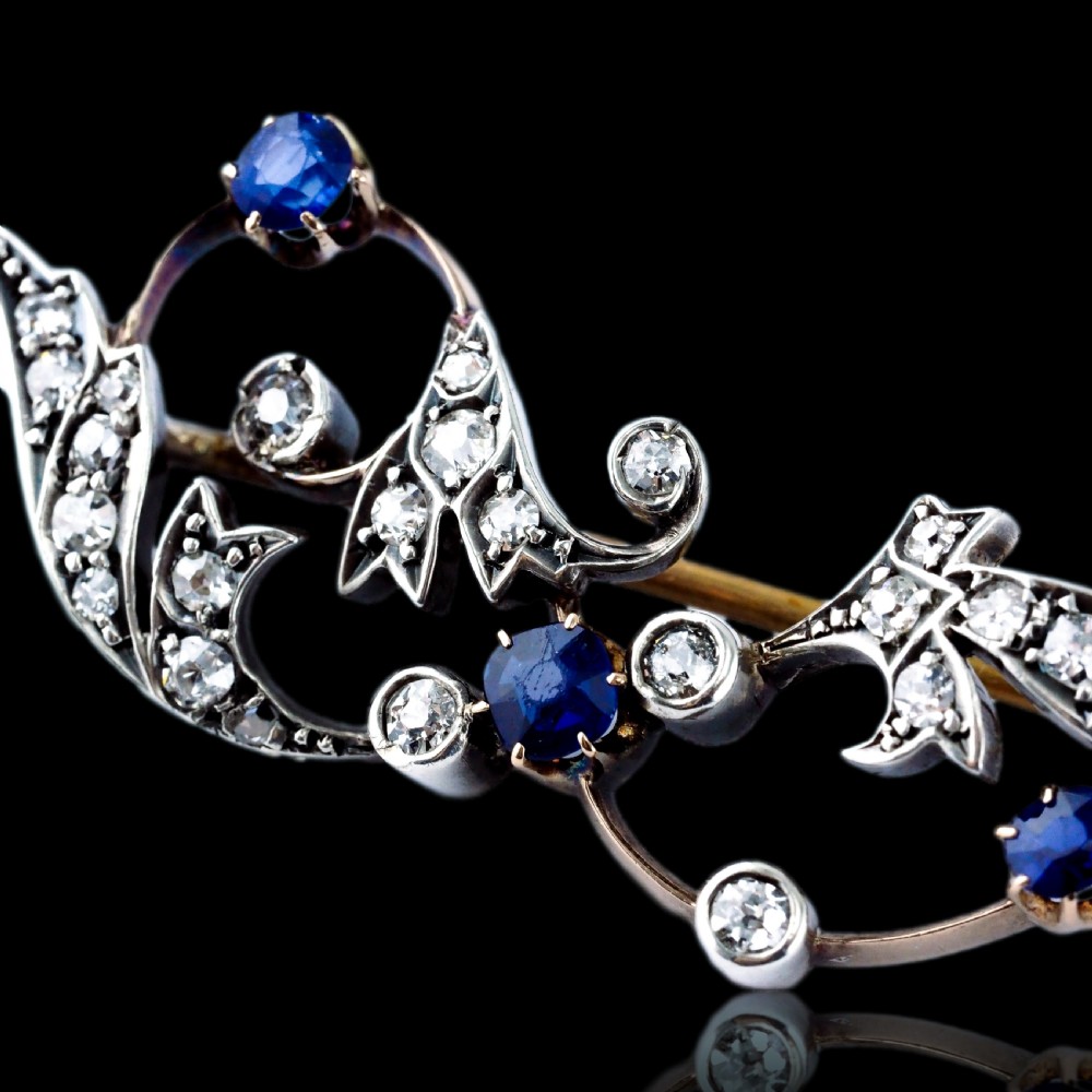 An antique Victorian foliate scroll brooch crafted in gold and silver, set with circular blue sapphires and accent diamonds. View X