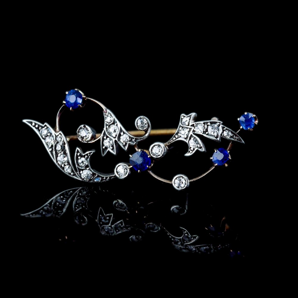 An antique Victorian foliate scroll brooch crafted in gold and silver, set with circular blue sapphires and accent diamonds. View XV