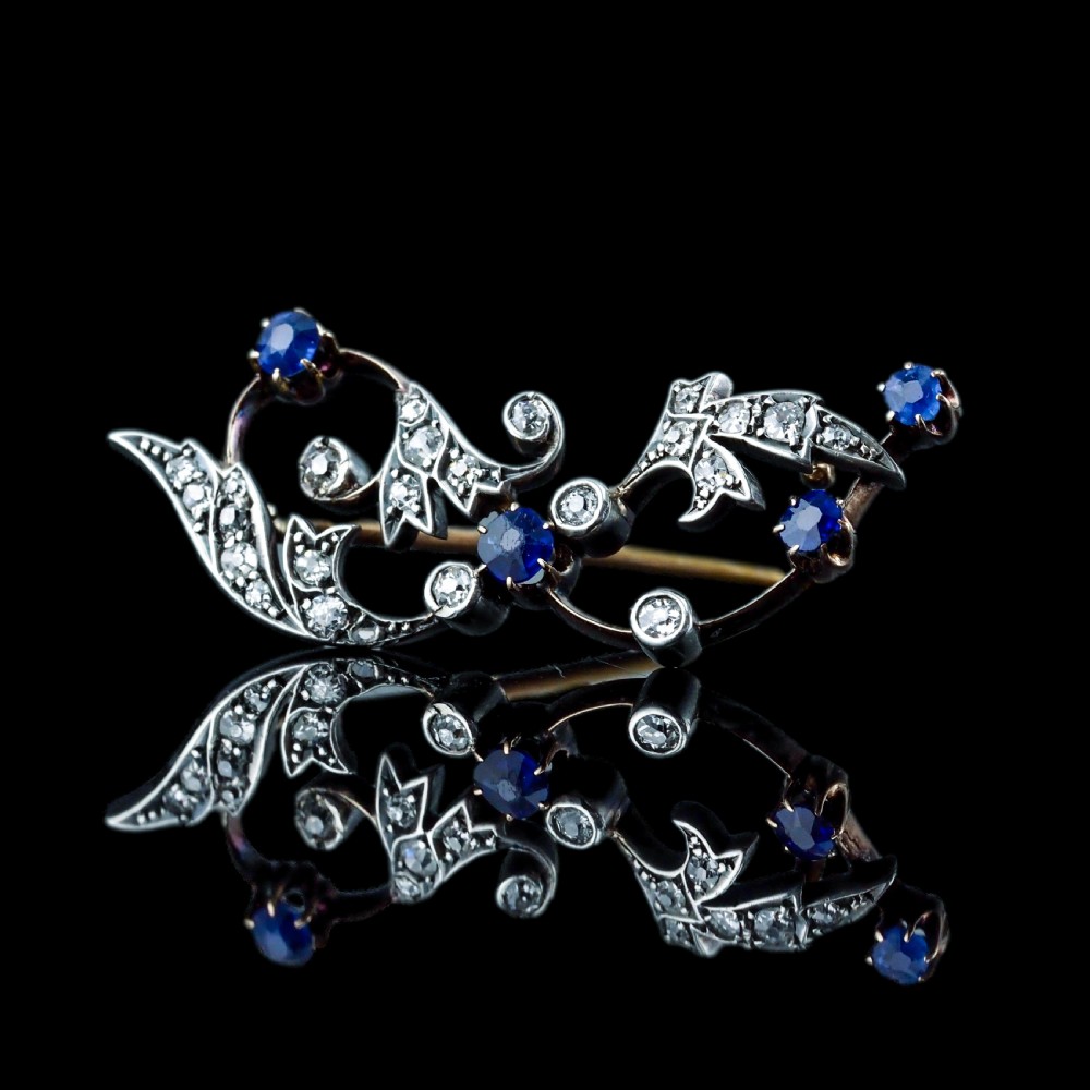 An antique Victorian foliate scroll brooch crafted in gold and silver, set with circular blue sapphires and accent diamonds. View XVI
