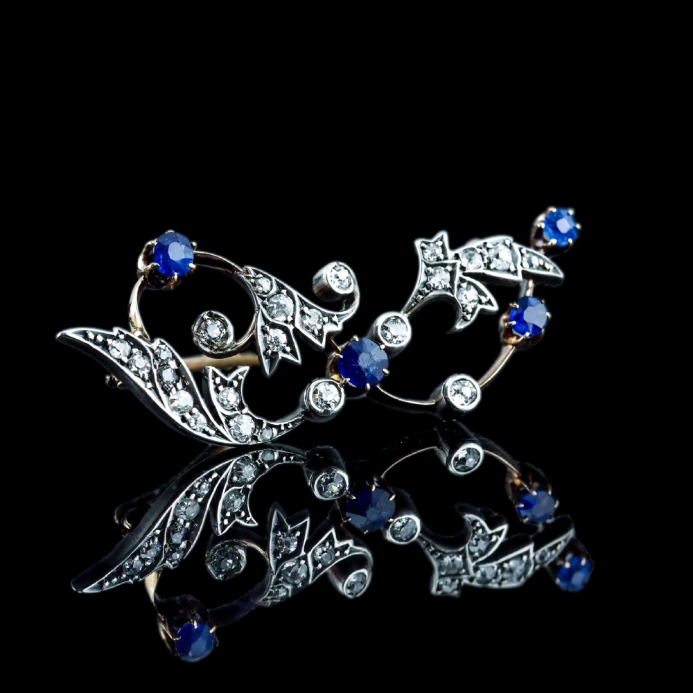An antique Victorian foliate scroll brooch crafted in gold and silver, set with circular blue sapphires and accent diamonds. View XIX