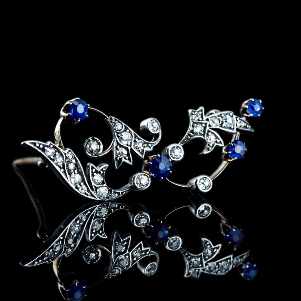 An antique Victorian foliate scroll brooch crafted in gold and silver, set with circular blue sapphires and accent diamonds. View XX
