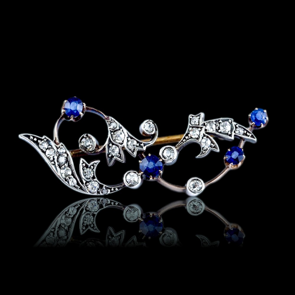 An antique Victorian foliate scroll brooch crafted in gold and silver, set with circular blue sapphires and accent diamonds. View XXI