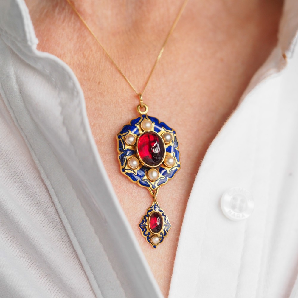An 18k yellow gold Victorian Holbeinesque pendant featuring a central red cabochon garnet surrounded by pearls, blue enamel, and an articulated gemstone drop. View VIII