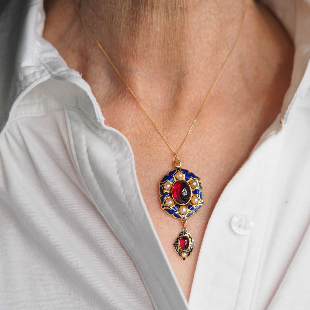 An 18k yellow gold Victorian Holbeinesque pendant featuring a central red cabochon garnet surrounded by pearls, blue enamel, and an articulated gemstone drop. View IX