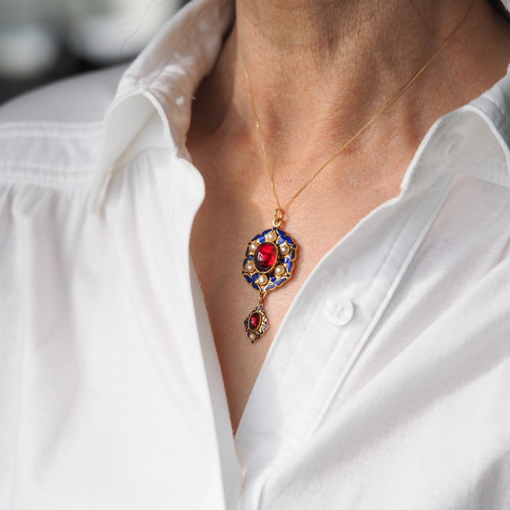 An 18k yellow gold Victorian Holbeinesque pendant featuring a central red cabochon garnet surrounded by pearls, blue enamel, and an articulated gemstone drop. View XI