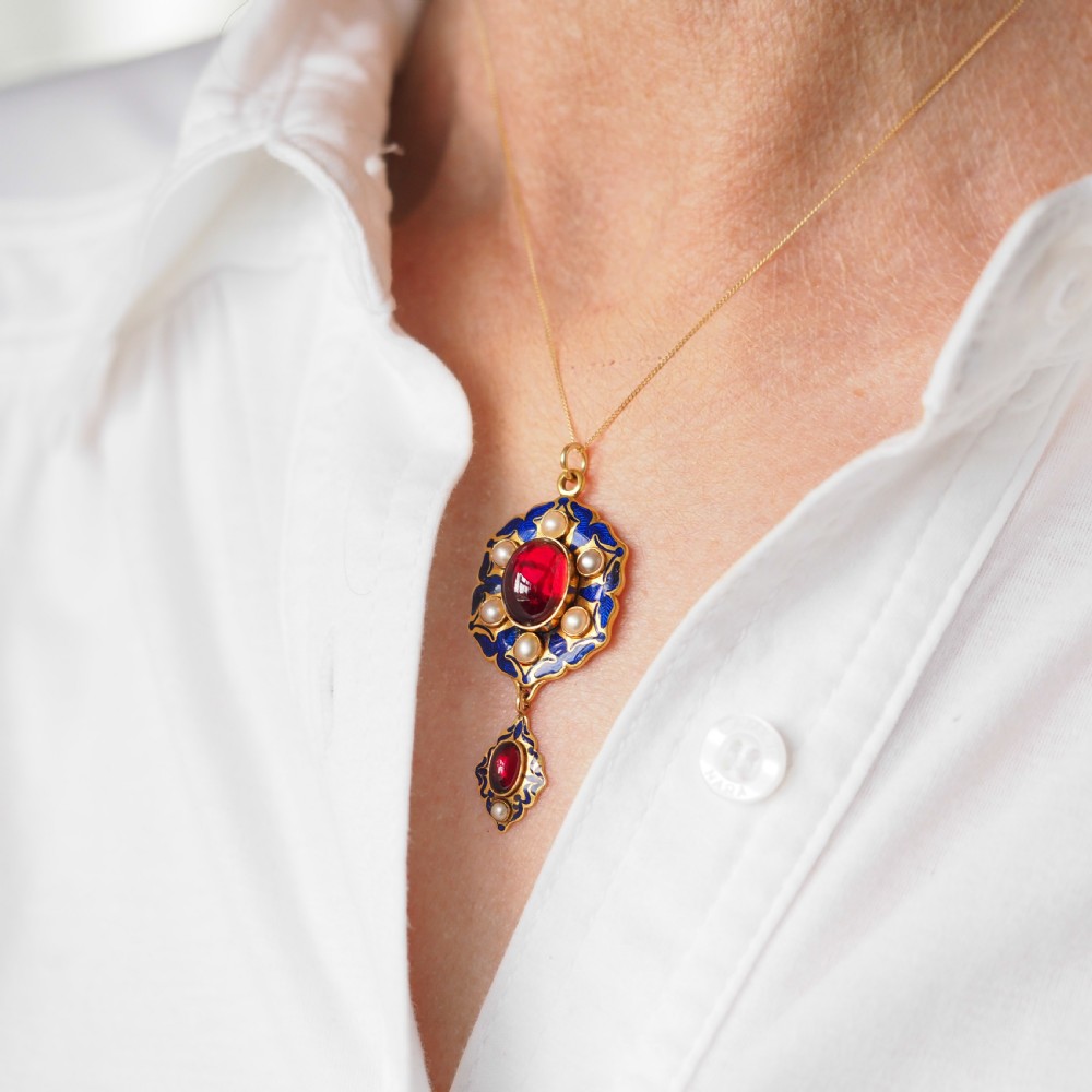 An 18k yellow gold Victorian Holbeinesque pendant featuring a central red cabochon garnet surrounded by pearls, blue enamel, and an articulated gemstone drop. View XII