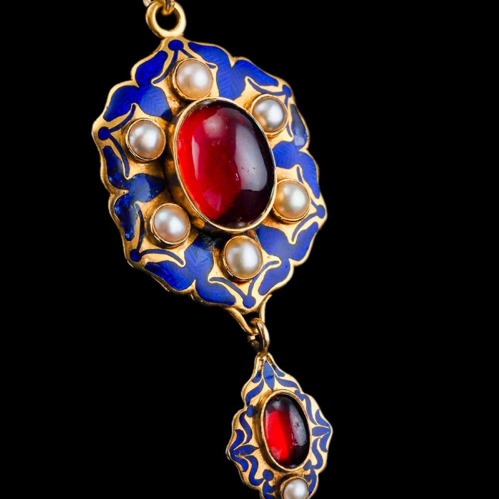 An 18k yellow gold Victorian Holbeinesque pendant featuring a central red cabochon garnet surrounded by pearls, blue enamel, and an articulated gemstone drop. View XIV