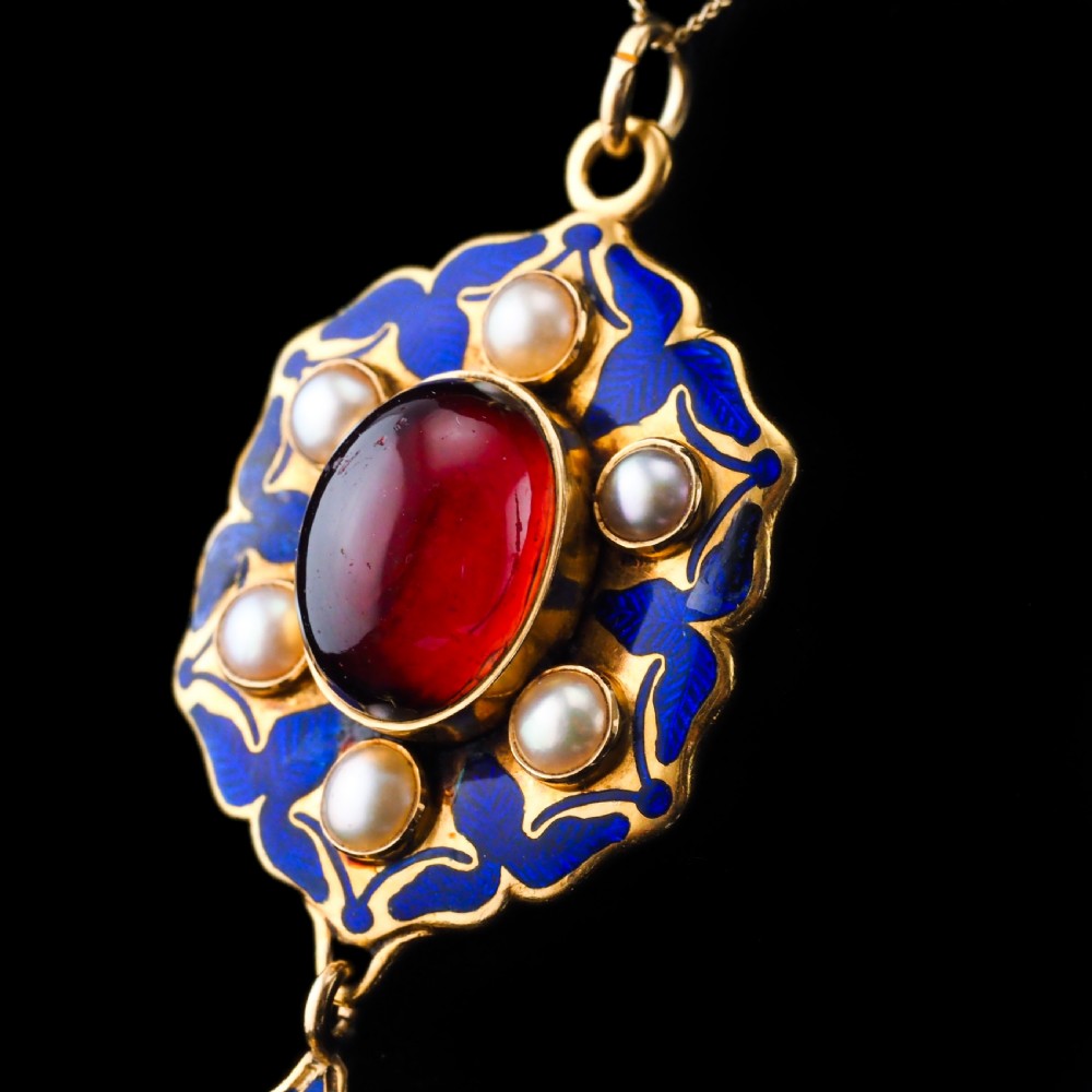 An 18k yellow gold Victorian Holbeinesque pendant featuring a central red cabochon garnet surrounded by pearls, blue enamel, and an articulated gemstone drop. View XV