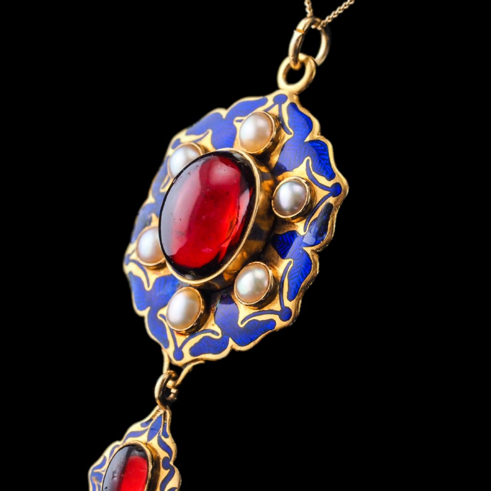 An 18k yellow gold Victorian Holbeinesque pendant featuring a central red cabochon garnet surrounded by pearls, blue enamel, and an articulated gemstone drop. View XVII