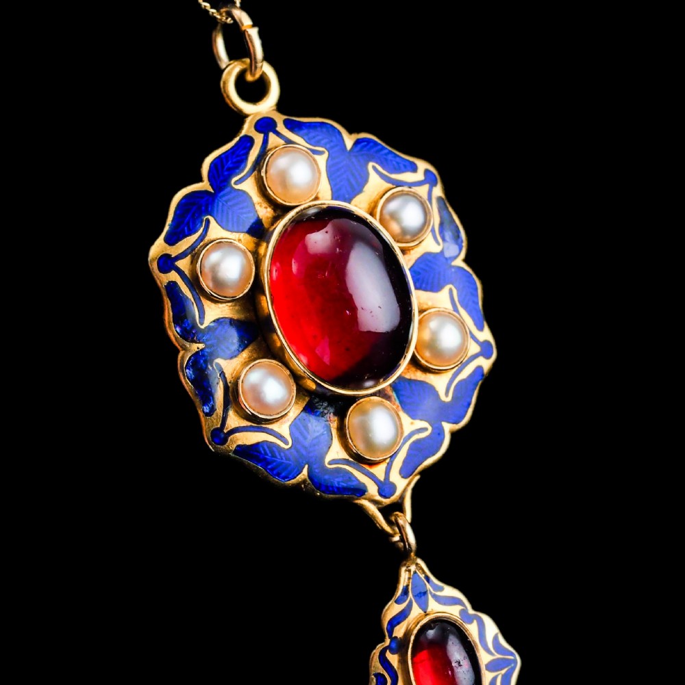 An 18k yellow gold Victorian Holbeinesque pendant featuring a central red cabochon garnet surrounded by pearls, blue enamel, and an articulated gemstone drop. View XVIII