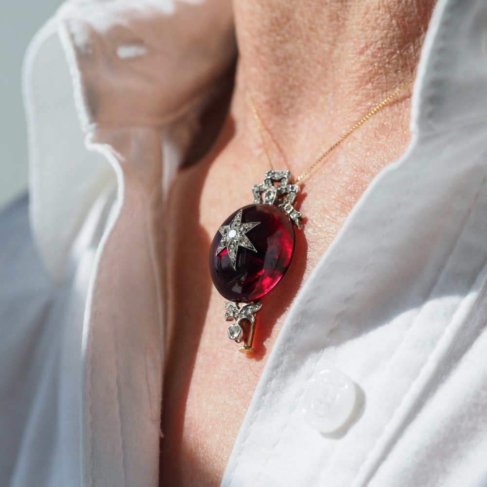 An antique Victorian oval garnet cabochon pendant brooch featuring an inset diamond star motif and a diamond-set ribbon bow top. View II
