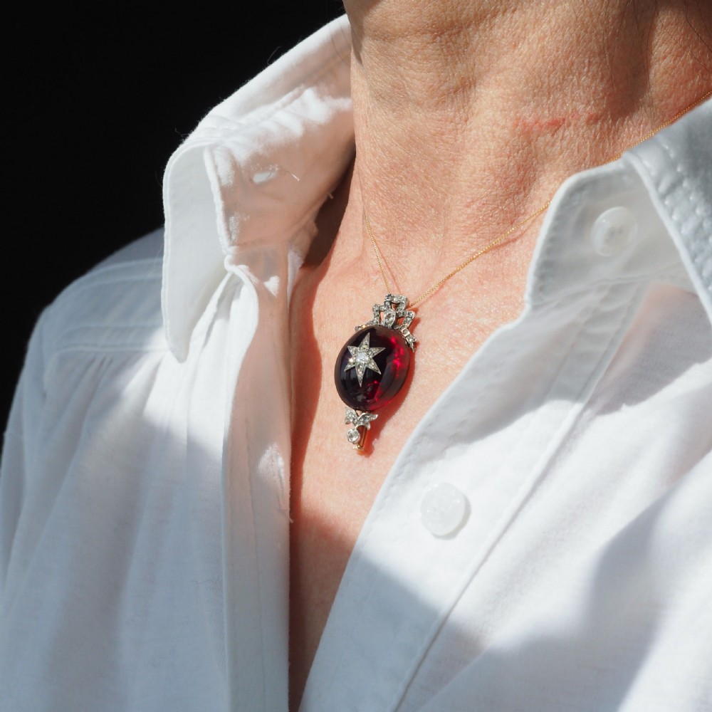 An antique Victorian oval garnet cabochon pendant brooch featuring an inset diamond star motif and a diamond-set ribbon bow top. View III