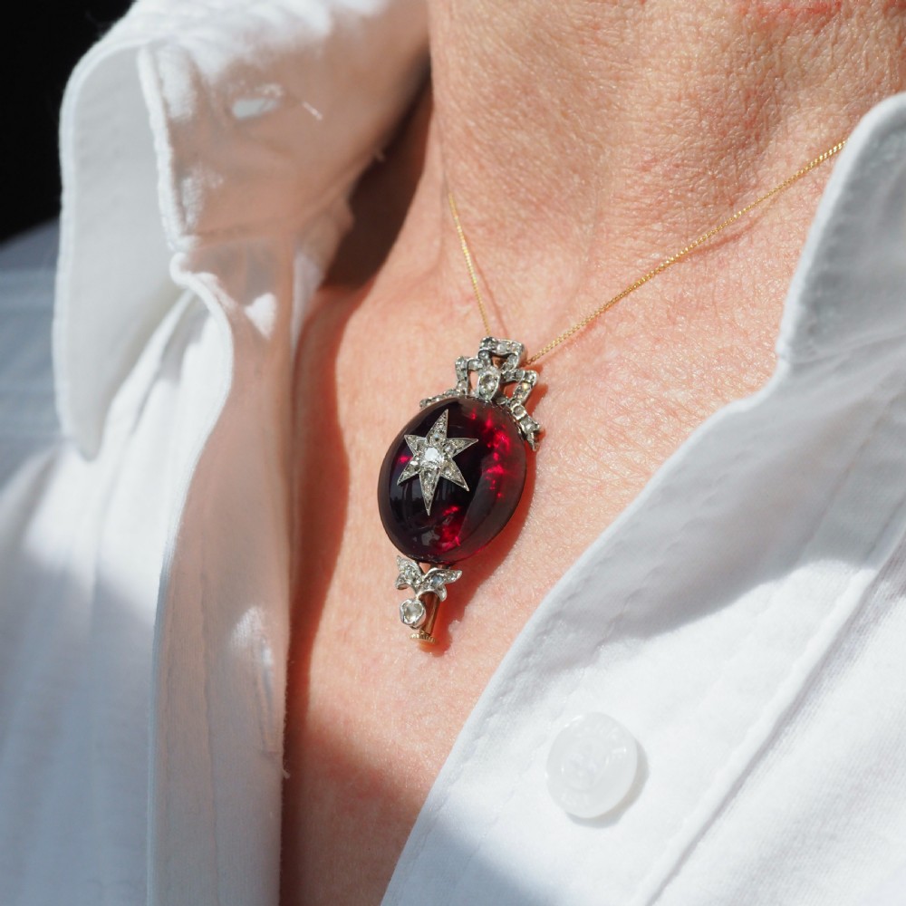 An antique Victorian oval garnet cabochon pendant brooch featuring an inset diamond star motif and a diamond-set ribbon bow top. View IV