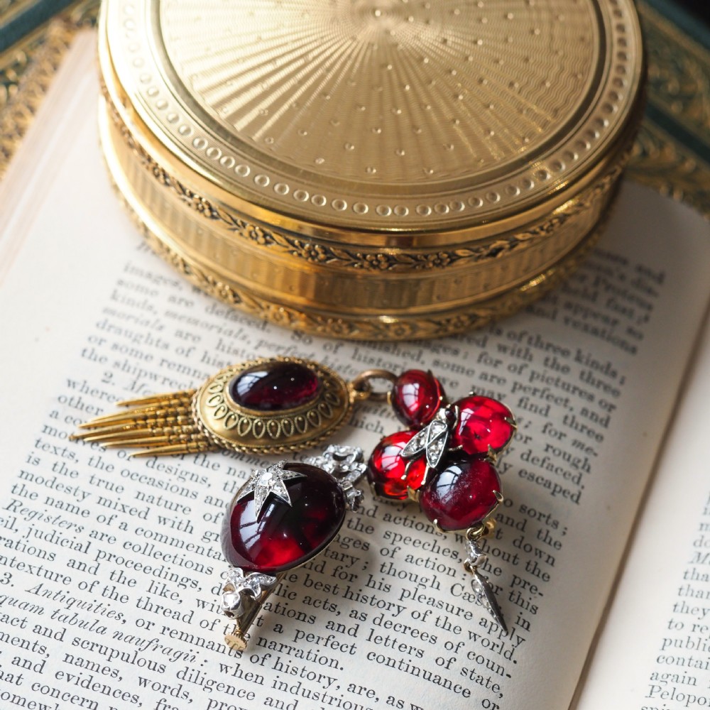 An antique Victorian oval garnet cabochon pendant brooch featuring an inset diamond star motif and a diamond-set ribbon bow top. View V