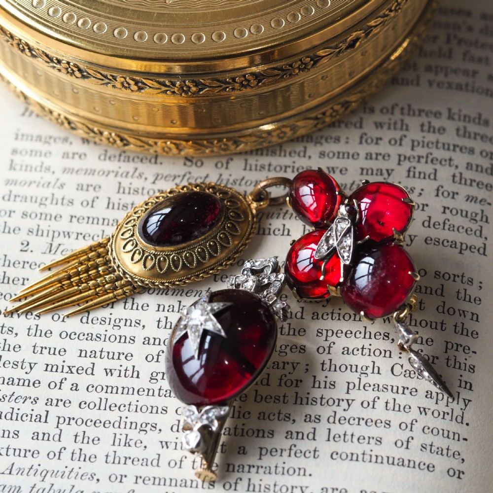 An antique Victorian oval garnet cabochon pendant brooch featuring an inset diamond star motif and a diamond-set ribbon bow top. View VI