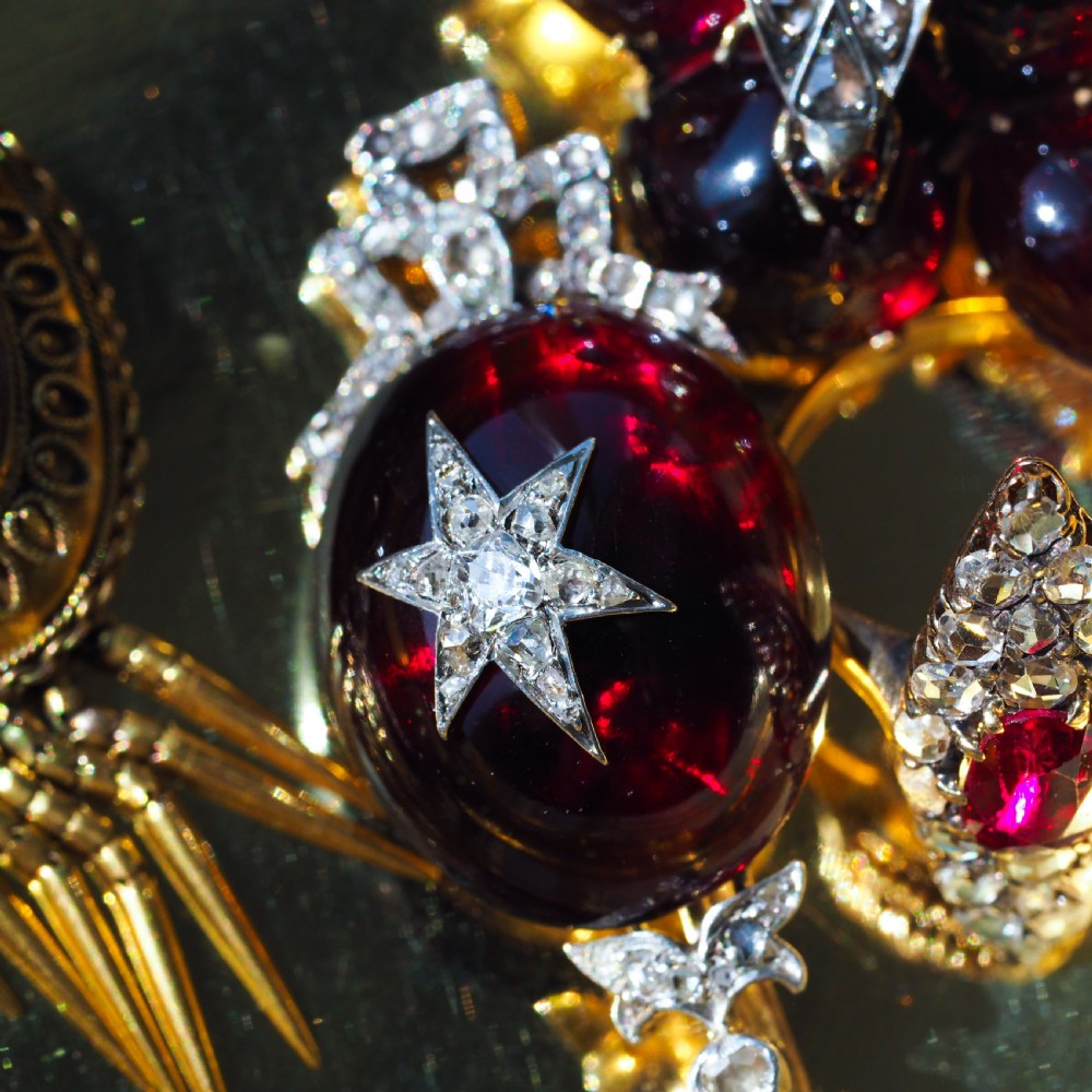 An antique Victorian oval garnet cabochon pendant brooch featuring an inset diamond star motif and a diamond-set ribbon bow top. View VII