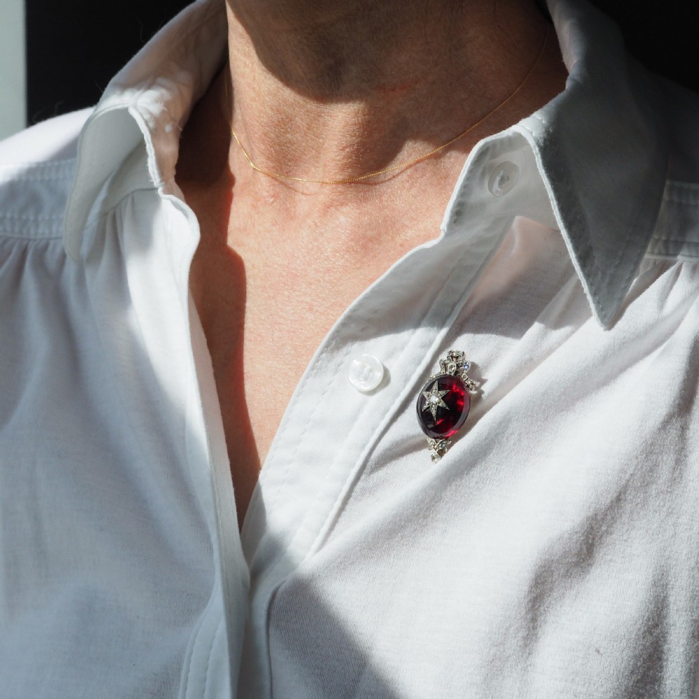 An antique Victorian oval garnet cabochon pendant brooch featuring an inset diamond star motif and a diamond-set ribbon bow top. View XV
