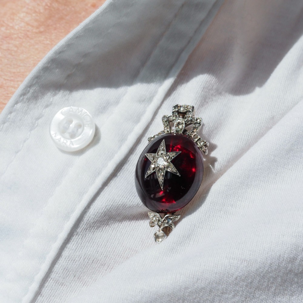 An antique Victorian oval garnet cabochon pendant brooch featuring an inset diamond star motif and a diamond-set ribbon bow top. View XVI