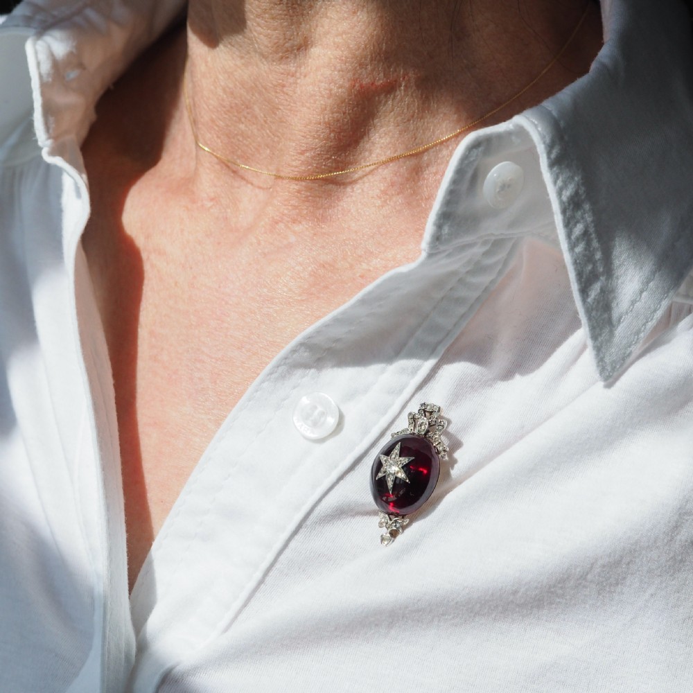 An antique Victorian oval garnet cabochon pendant brooch featuring an inset diamond star motif and a diamond-set ribbon bow top. View XVII