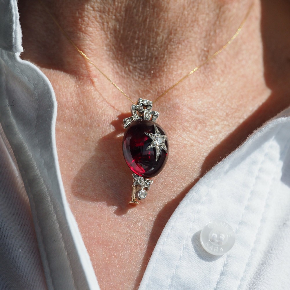 An antique Victorian oval garnet cabochon pendant brooch featuring an inset diamond star motif and a diamond-set ribbon bow top. View XVIII