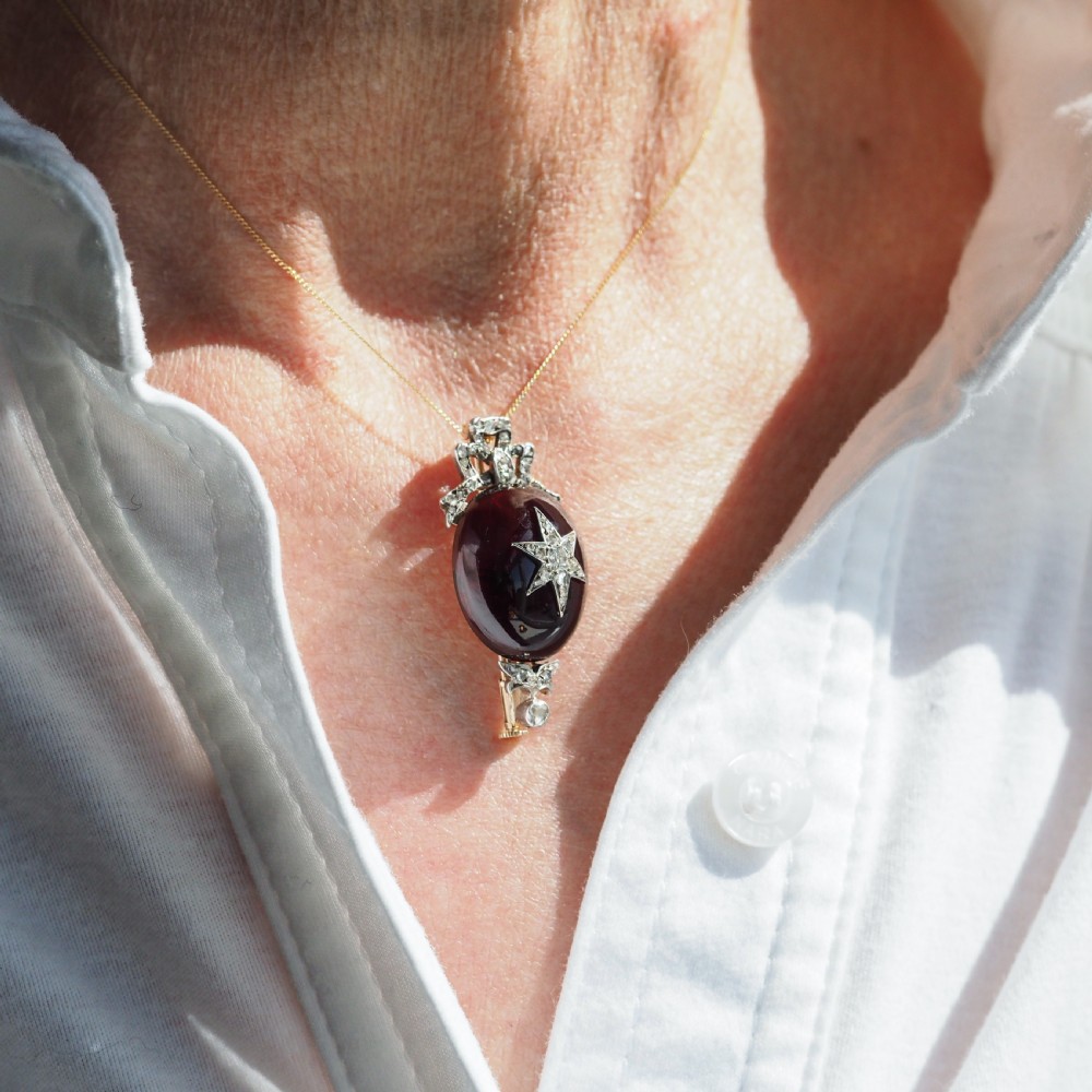 An antique Victorian oval garnet cabochon pendant brooch featuring an inset diamond star motif and a diamond-set ribbon bow top. View XIX