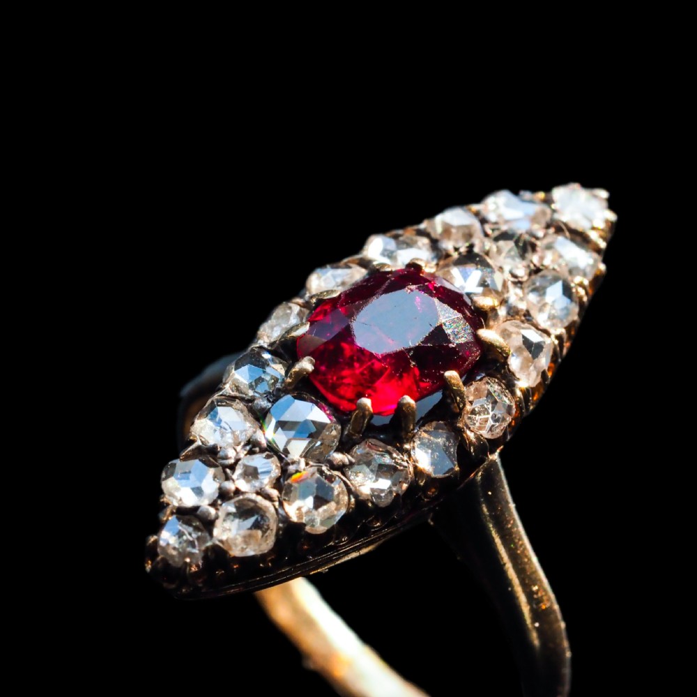 An antique late-nineteenth-century French 18k gold navette cluster ring featuring a central oval red ruby surrounded by multiple rose-cut diamonds. View VI
