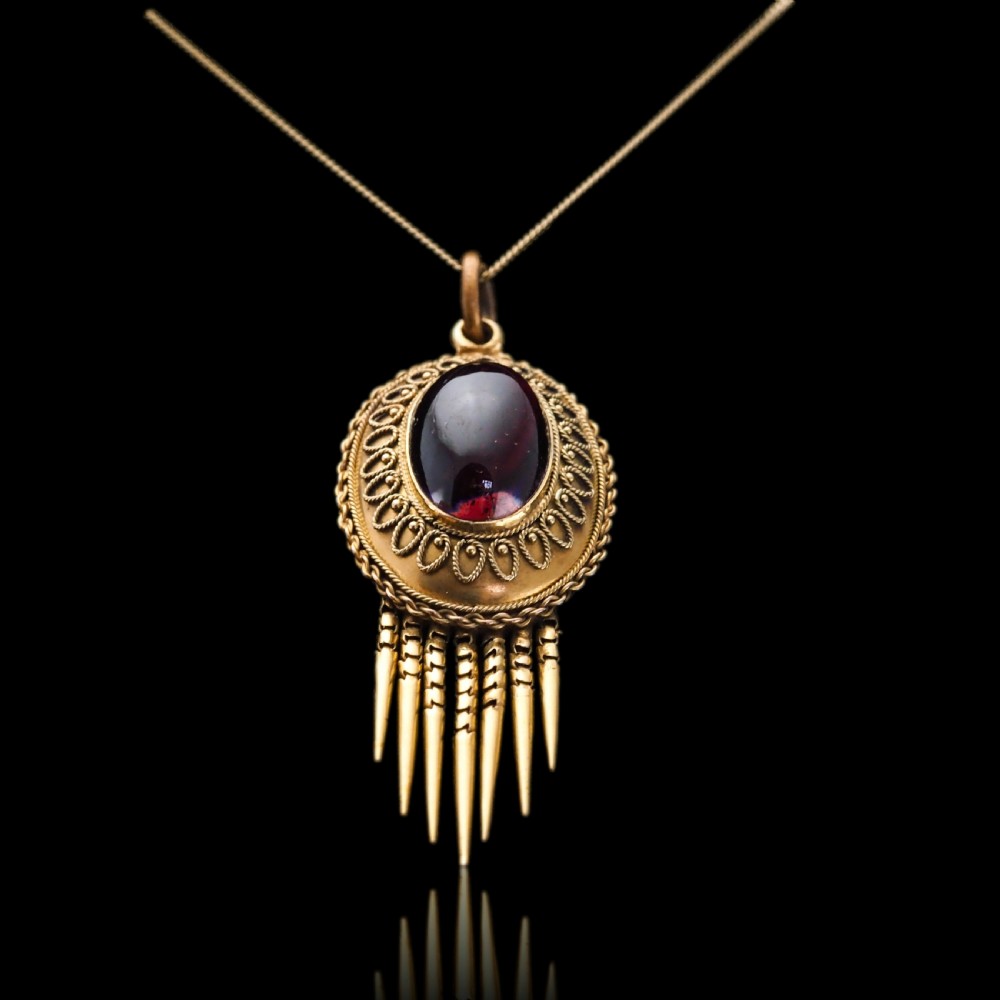 A Victorian 15ct gold oval Etruscan Revival pendant set with a central cabochon garnet and decorated with fine wirework and hanging spike tassels. View IV