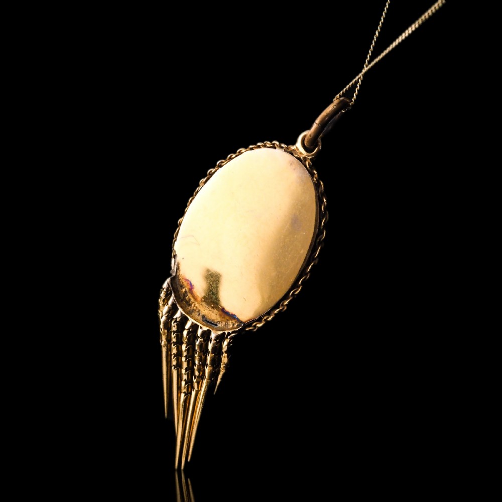 A Victorian 15ct gold oval Etruscan Revival pendant set with a central cabochon garnet and decorated with fine wirework and hanging spike tassels. View VI