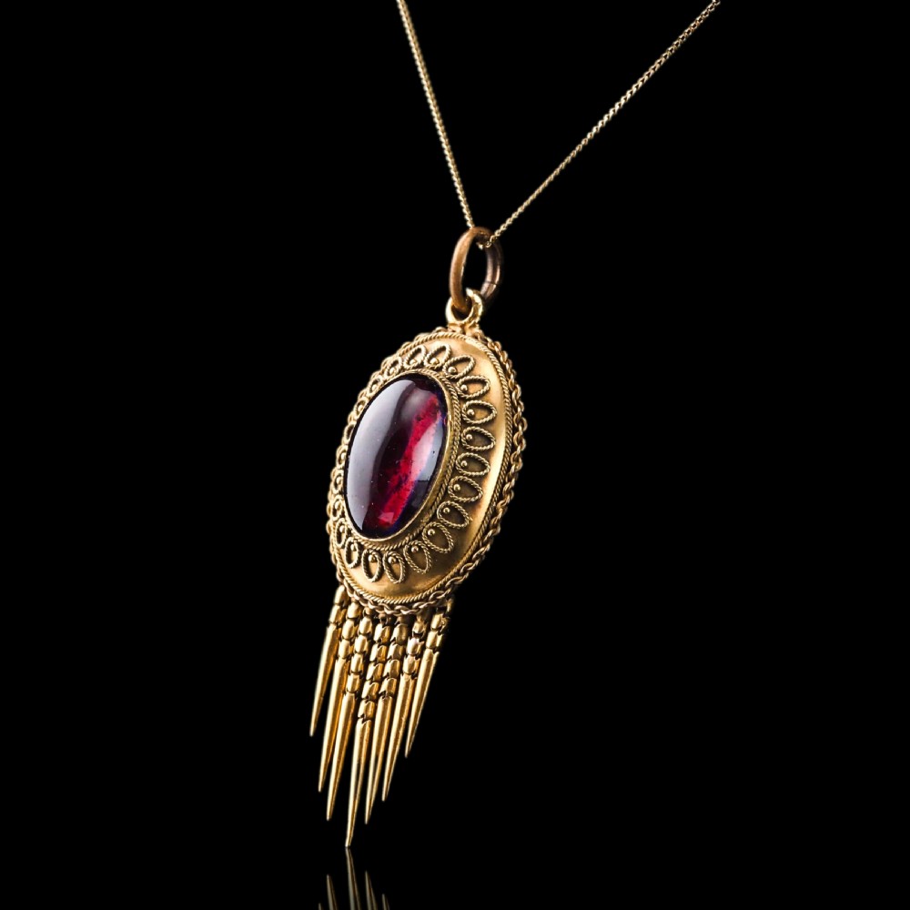 A Victorian 15ct gold oval Etruscan Revival pendant set with a central cabochon garnet and decorated with fine wirework and hanging spike tassels. View VII