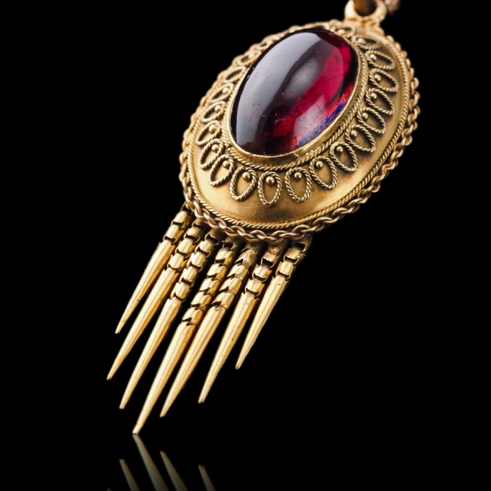 A Victorian 15ct gold oval Etruscan Revival pendant set with a central cabochon garnet and decorated with fine wirework and hanging spike tassels. View VIII