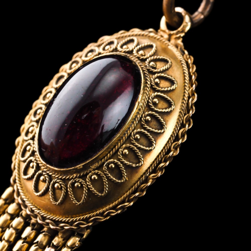 A Victorian 15ct gold oval Etruscan Revival pendant set with a central cabochon garnet and decorated with fine wirework and hanging spike tassels. View IX