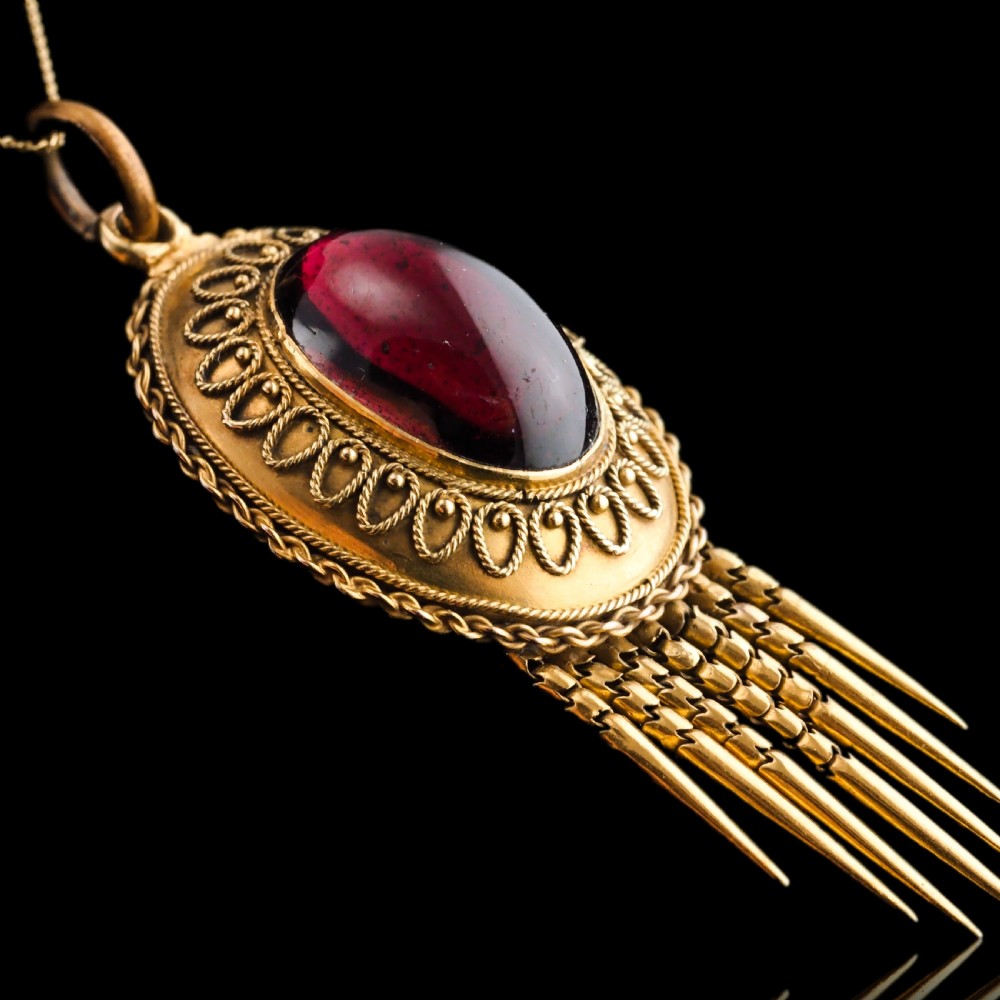 A Victorian 15ct gold oval Etruscan Revival pendant set with a central cabochon garnet and decorated with fine wirework and hanging spike tassels. View X