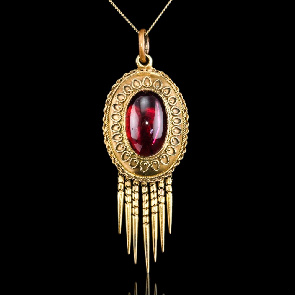 A Victorian 15ct gold oval Etruscan Revival pendant set with a central cabochon garnet and decorated with fine wirework and hanging spike tassels. View XI