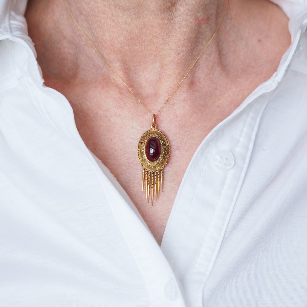A Victorian 15ct gold oval Etruscan Revival pendant set with a central cabochon garnet and decorated with fine wirework and hanging spike tassels. View XII