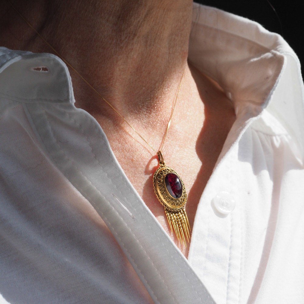 A Victorian 15ct gold oval Etruscan Revival pendant set with a central cabochon garnet and decorated with fine wirework and hanging spike tassels. View XIII